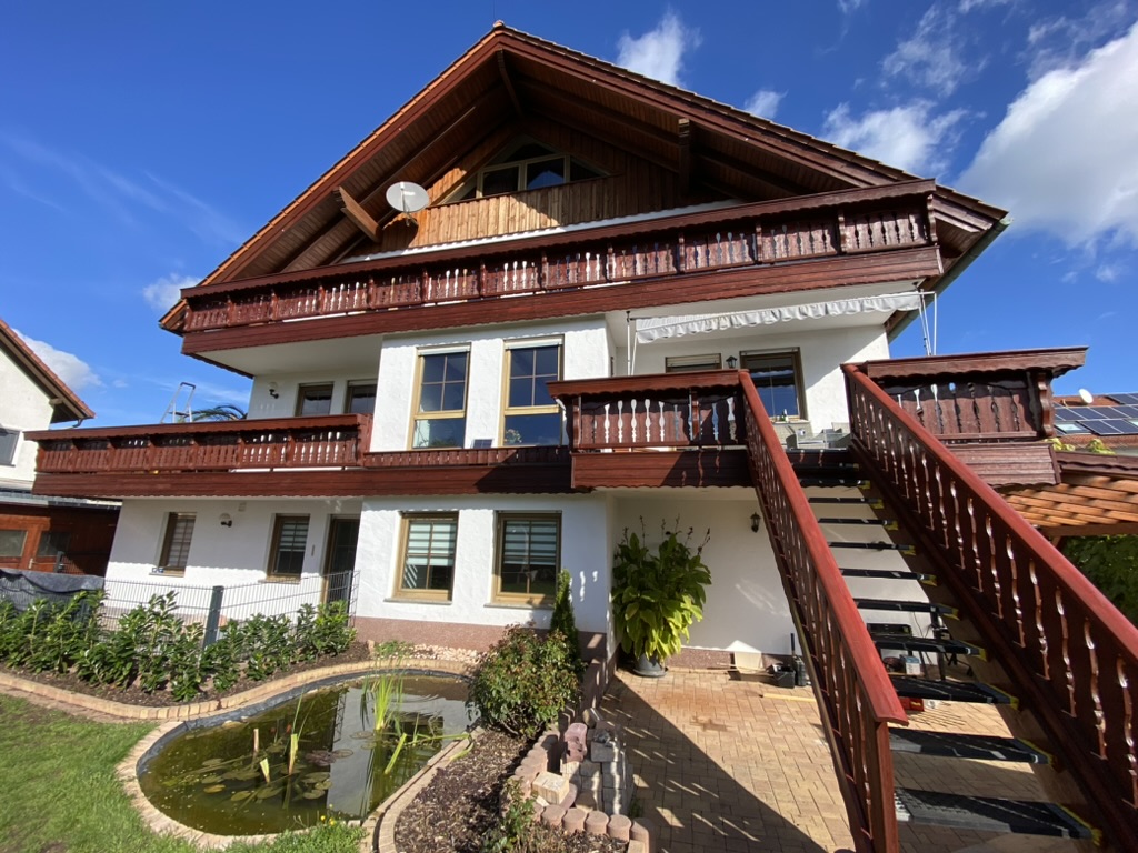 Helle Hausfassade mit Holzbalkonen und Außentreppe